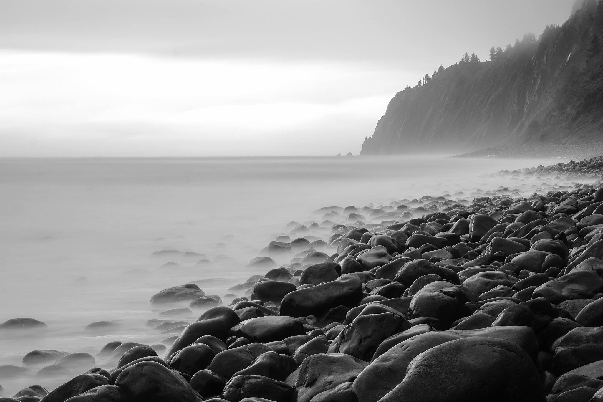 A picture of smooth rocks by the ocean taken with a long exposure to make the water look like mist.