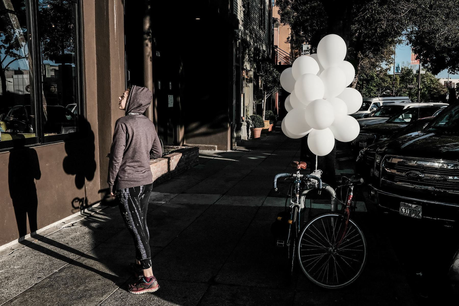 A woman looks into a shop window. Behind her is a bike with a bouquet of white balloons.