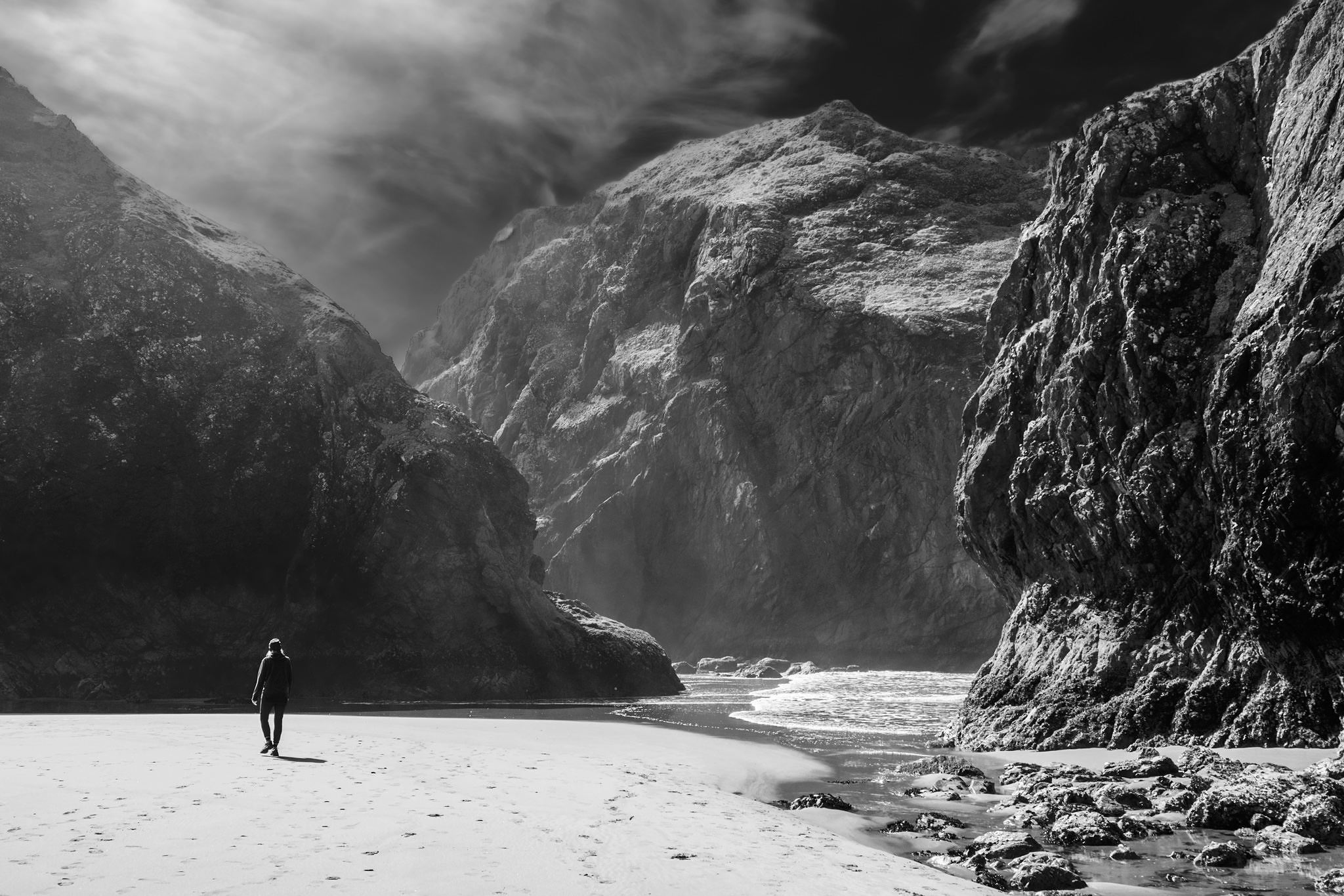 Monochrome. A person wanders through a misty canyon surrounded by large ocean rocks.