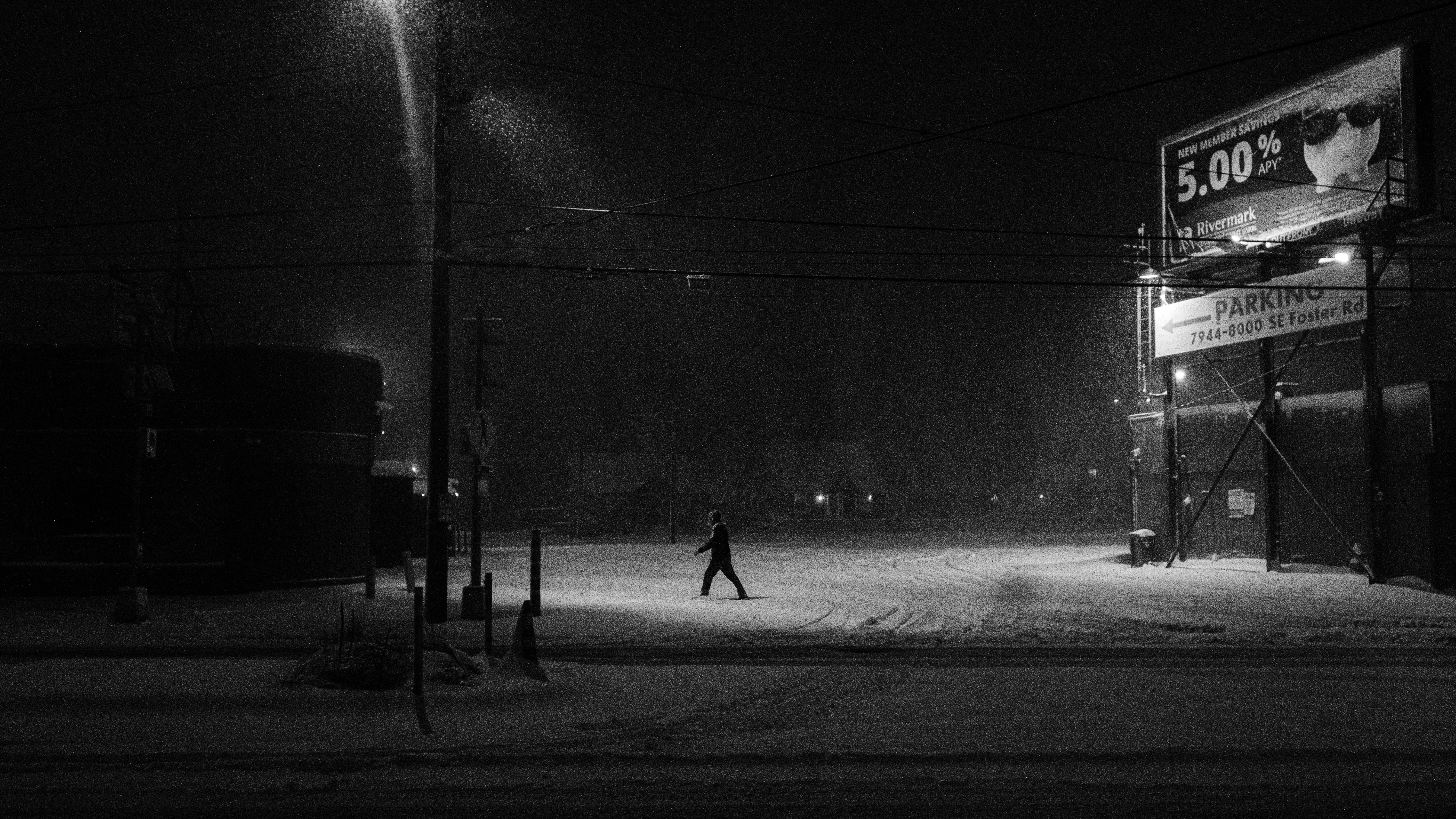 Monochrome. Two people cross a street at night during a snowstorm.