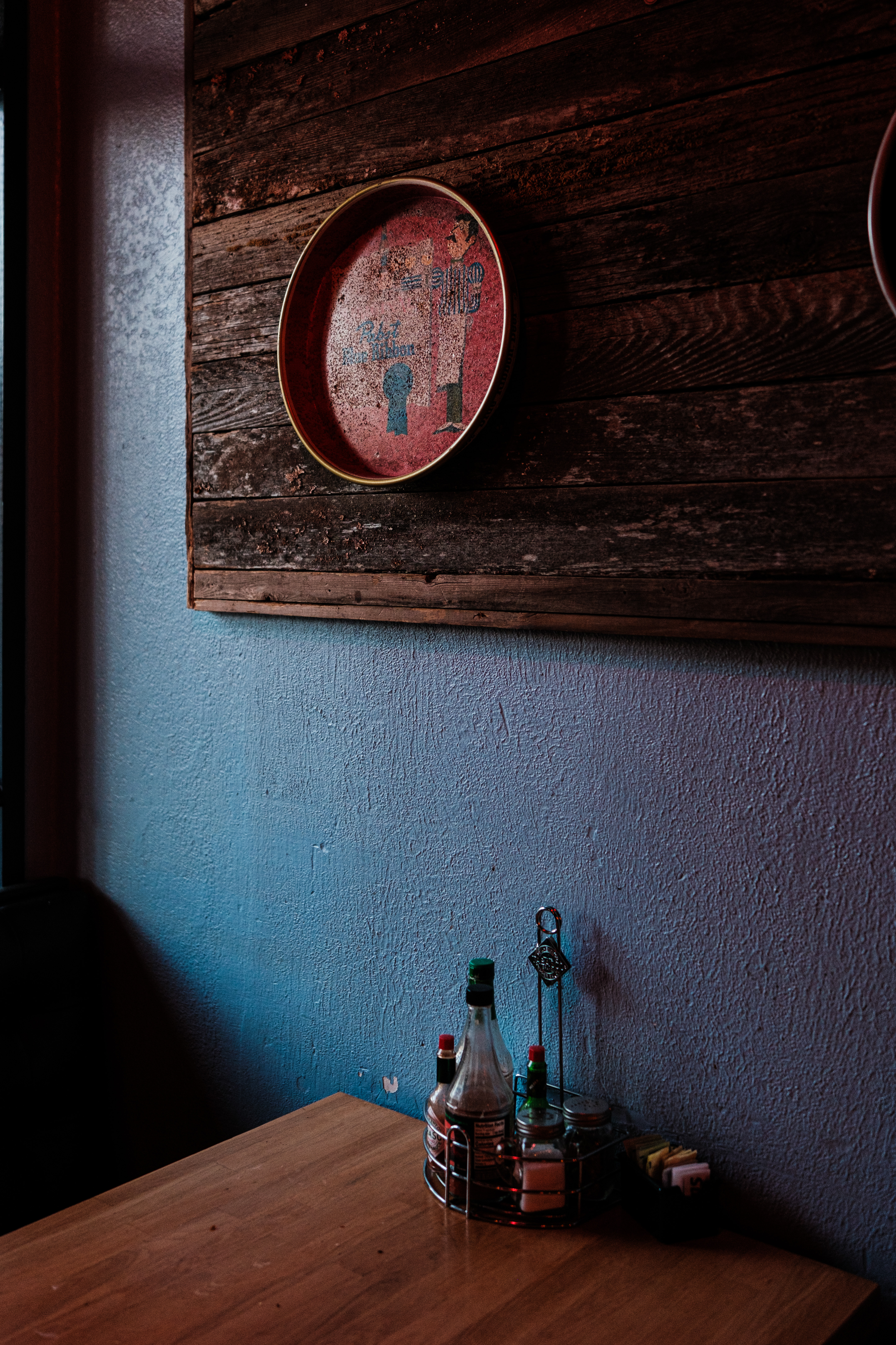 A wooden table in a cafe in partial shadows. Blue wall. Decorative red enamel plate.