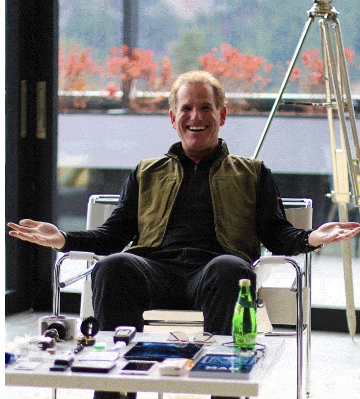 Picture of a smiling man sitting in a vest with a table full of stuff in front of him