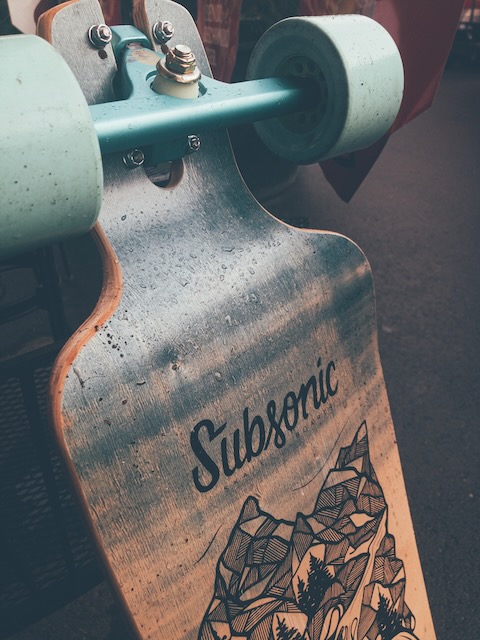 Closeup of longboard trucks with light blue 90mm wheels attached and the Subsonic logotype on the deck