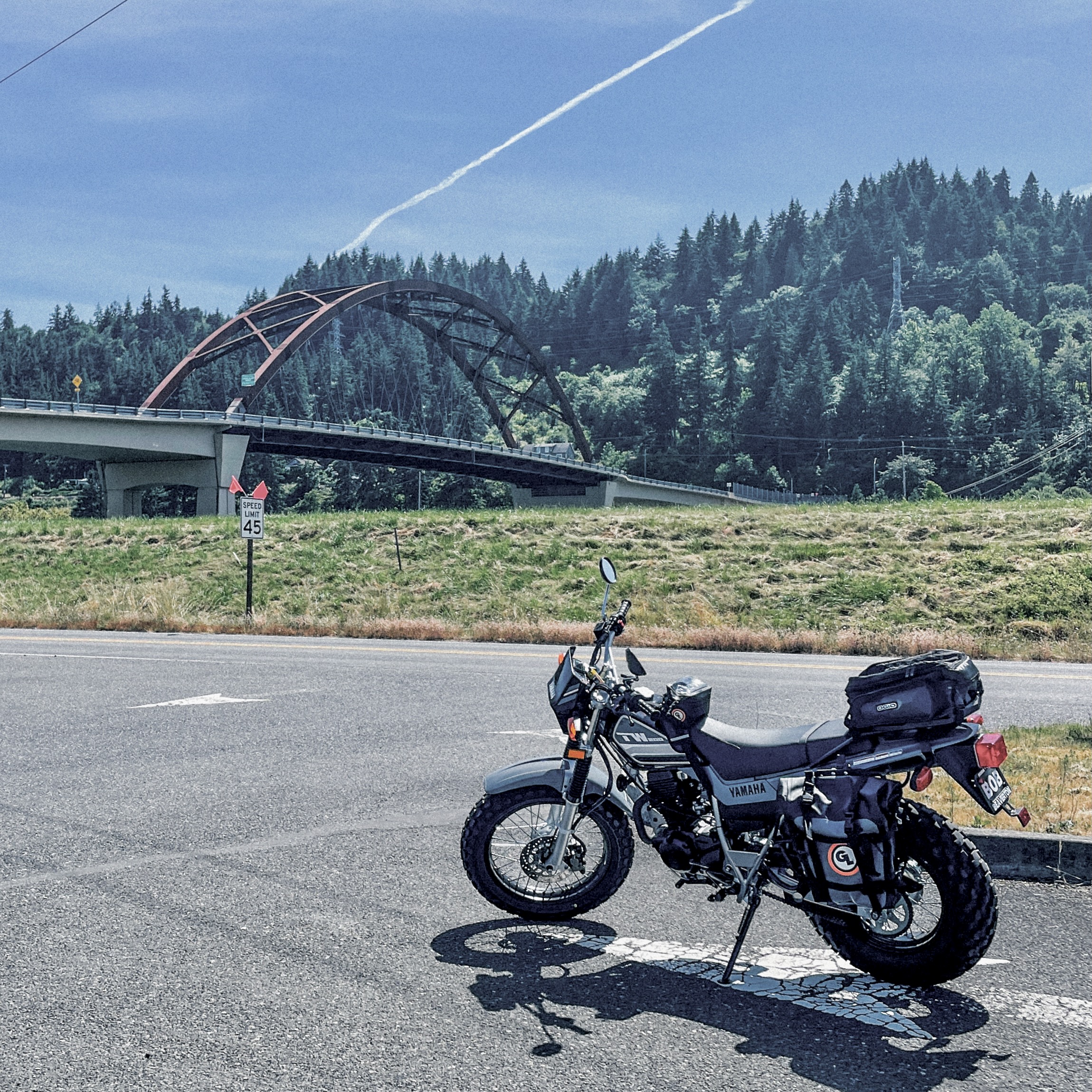 A Yamaha TW200 parked in front of a suspension bridge on a sunny day.