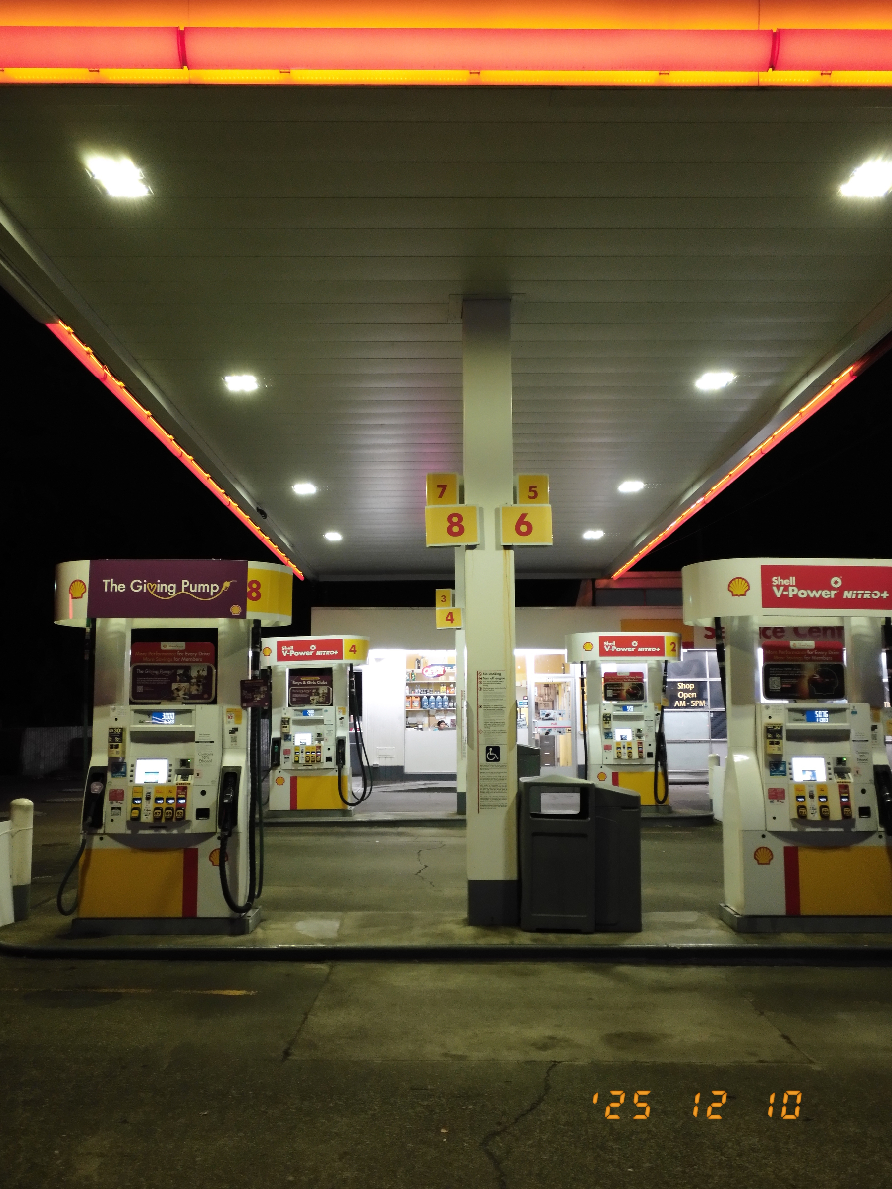 A well-lit gas station at night features multiple fuel pumps with signs and digital displays.