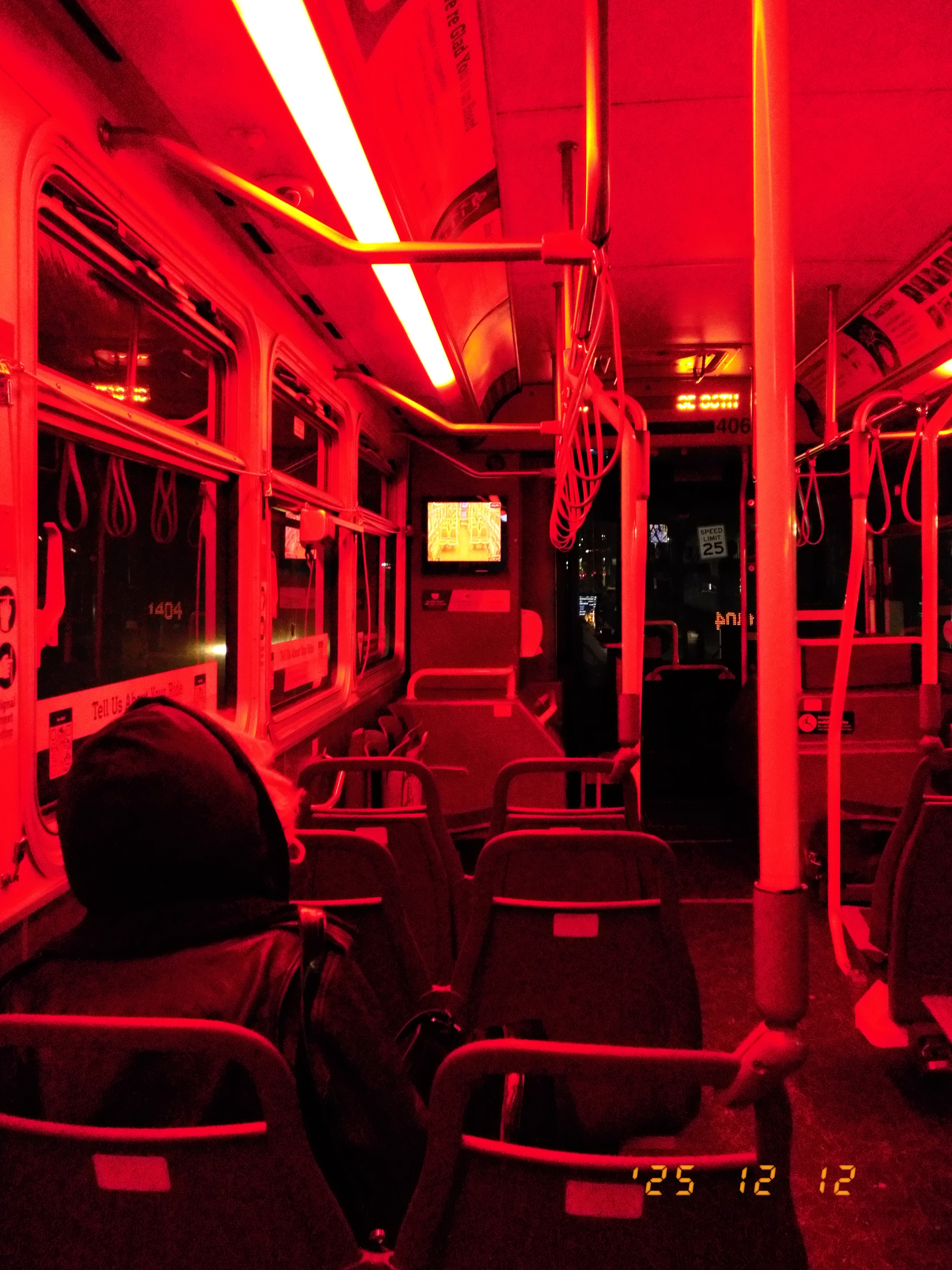 A dimly lit bus interior is illuminated by red lights, with a few passengers seated and a small screen displaying an image.
