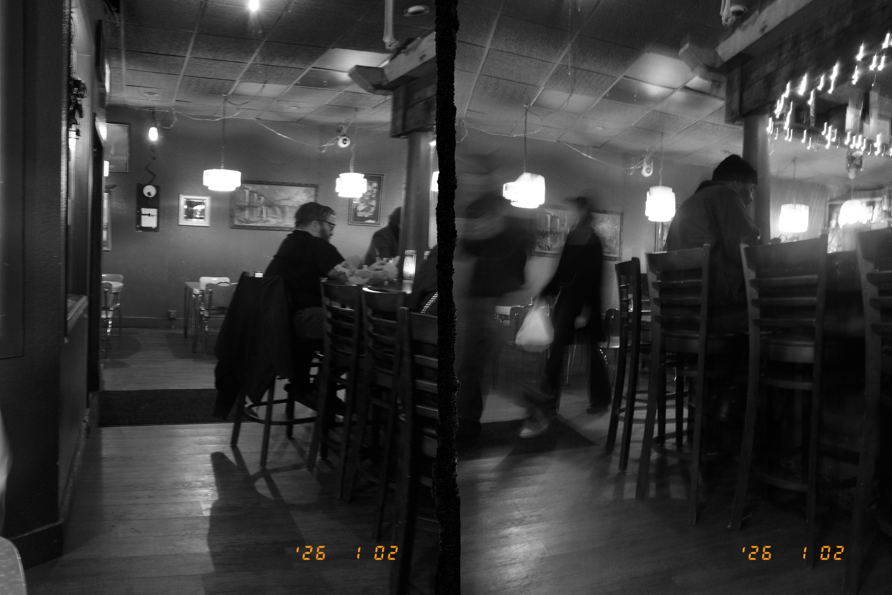 In a dimly lit restaurant, people are seated and standing around a bar counter with ambient light fixtures overhead.